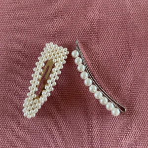 Hårspännen med pärlor - Två  hårspännen dekorerade med vita pärlor. Det ena spännet har en rektangulär form med tätt placerade pärlor, medan det andra har en böjd design med en rad av större pärlor. Säljer båda för 50kr eller var för sig för 30kr