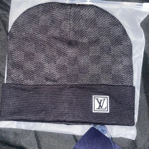 Svart mössa med logotyp - Snygg svart mössa med en diskret logotyp framtill. Mössan har en ribbad kant och är perfekt för kyligare dagar. Den är stilren och passar till många olika outfits.