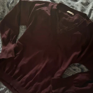 Vinröd v-ringad tröja - Orsay - Mysig vinröd tröja från Orsay med v-ringning och fina spetsdetaljer vid halsen. Långärmad modell i mjukt material, snygg till jeans eller kjol.