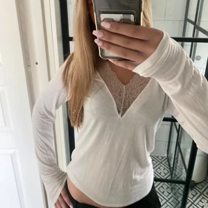Vit långärmad topp med spetsdetalj - Säljer en vit långärmad topp med snygg v-ringning och spetsdetalj vid urringningen. Toppens material känns lätt och mjukt, typ som topparna från intimissmi. Toppen är från Ullared och är använd men i fint skick