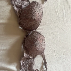 Rosa spets-bh med blommönster 70A - Söt bh i ljusrosa med blommig spets och vadderade kupor. Justerbara axelband och fina spetsdetaljer längs kanterna. Materialet är mjukt och stretchigt med 90% polyamid och 10% elastan för skön passform.