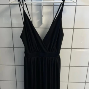 Svart långklänning med slits - Snygg svart långklänning med djup v-ringning och öppen rygg. Klänningen har hög slits framtill och inbyggd body. Passar XS/S. Använd 2 gånger 