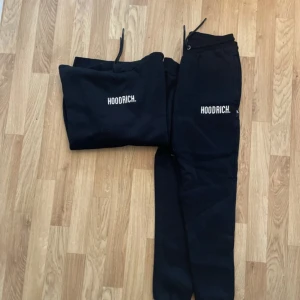 Svart hoodie från Hoodrich med tryck - Svart hoodie från Hoodrich med vit logga på bröstet. Klassisk modell med huva, snörning och stor magficka. Mjuk insida och ribbade muddar. Perfekt för chill eller streetwear-stil.