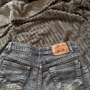 Blå jeansshorts från 97 Jeans - Snygga blå jeansshorts från 97 Jeans med slitna detaljer och rå kant nedtill. Klassisk femficksmodell med ljusa tvättade partier och synliga sömmar. Perfekt för dig som gillar en avslappnad och cool stil.