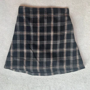 Rutig svart kjol från SHEIN - Kort kjol från SHEIN i svart med rutigt mönster i beige och vitt. Kjolen har en rak passform och resår i midjan för extra komfort. Perfekt för dig som gillar en klassisk men trendig stil.