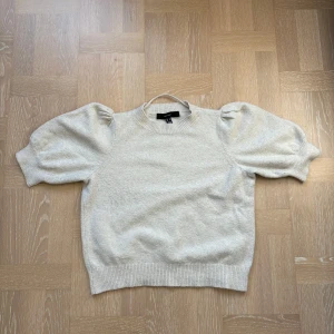 Beige stickad tröja - Superfin beige stickad tröja från Vero Moda med korta puffärmar och ribbade muddar. Tröjan har en rund halsringning och passar perfekt till både jeans och kjol.
