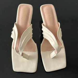 Vita sandaler med fyrkantig tå från SHEIN - Stilrena vita sandaler från SHEIN med fyrkantig tå och låg klack. Skorna har breda remmar i syntetmaterial och en unik design framtill. Perfekta för dig som gillar trendiga och minimalistiska skor med en modern twist.