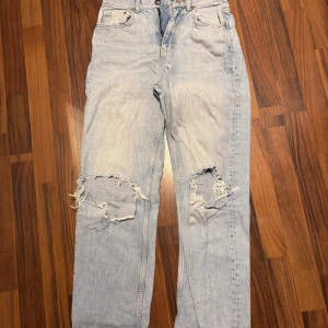 Ljusblå ripped jeans från Gina Tricot - Säljer ett par ljusblå jeans från Gina Tricot med snygga slitningar över knäna. Klassisk femficksmodell i denim med raka ben och normal passform. Perfekta för en avslappnad och trendig look. Storlek 36. Raka ben. Aldrig använda. 