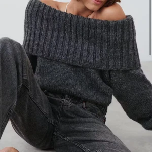 Grå offshoulder stickad tröja - Supermysig grå stickad tröja med bred ribbad offshoulder-krage. Tröjan har lång ärm och en loose fit som ger en chill vibe. Perfekt för lager på lager och att styla med jeans eller kjol. Tjockt garn och ribbade muddar för extra komfort.