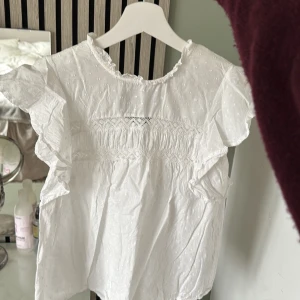 Vit blus med volangärmar från vero Moda  - Supersöt vit blus med volangärmar och broderade detaljer. Perfekt för en fräsch och söt look, passar till både jeans och kjol.