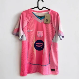 FC Barcelona rosa matchtröja Nike - Snygg FC Barcelona fotbollströja i rosa med vita och lila detaljer. Tröjan har korta ärmar, klubbmärke och Nike-logga på bröstet samt Spotify som sponsor. Nummer 10 och Lamine Yamal på ryggen. Tillverkad i lätt och ventilerande material.