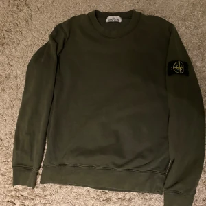 Stone Island grön sweatshirt - Säljer en grön crewneck sweatshirt från Stone Island med klassisk patch på vänster ärm. Tröjan har rund hals, långa ärmar och ribbade muddar. Perfekt för dig som gillar streetwear och vill ha något stilrent med ikonisk logga.