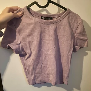 Ljuslila croppad topp från Zara - En enkel och stilren ljuslila croppad topp från Zara. Toppen har korta ärmar och rund halsringning, perfekt att matcha med jeans eller kjol. Mjuk bomullskänsla och passar dig som gillar en avslappnad men trendig look.