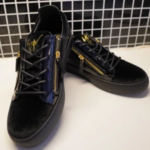 Giuseppe Zanotti - Snygga svarta sneakers i mocka och lack från Giuseppe Zanotti med guldfärgade dragkedjor och detaljer. Skorna har snörning, platt sula och rund tå. Guldlogga på plösen och metallic-detalj bak ger en lyxig vibe. . Helt nya , påse följer med , storlek 41 & 42 , skriv för mer 