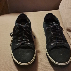 Svarta sneakers från Lanvin i mocka - Snygga svarta sneakers från Lanvin med ovandel i mocka och klassisk vit sula. Skorna har rund tå, snörning med färgade skosnören och diskreta sömdetaljer. Perfekta för dig som gillar stilrena och exklusiva sneakers med en lyxig känsla.