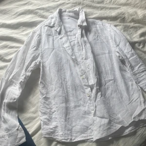 Vit linneskjorta från Zara - Klassisk vit skjorta från Zara i 100% linne. Skjortan har lång ärm, knappar framtill och en avslappnad passform. Perfekt för en clean och fräsch look, lätt att styla med jeans eller shorts.