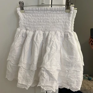 Söt Vit volangkjol med broderade detaljer🫰🏻 - Supersöt vit kortkjol med bred smock i midjan och flera lager volanger. Kjolen har broderade blommor och fina spetskanter! Väldigt stretchig i midjan så passar många. Står ej vart den är ifrån🙈
