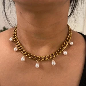 Guldigt halsband med pärldroppar - Chunky halsband i guldton med breda länkar och hängande vita pärldroppar. Perfekt statement piece som ger en lyxig och trendig vibe. Snyggt att matcha med både basic och mer dressade outfits.