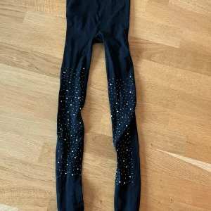 Svarta leggings med glittriga stenar - Svarta strumpbyxor med tight passform och glittriga stenar i olika storlekar längs benen. Perfekta för dig som vill sticka ut lite extra. Mjukt och stretchigt material som sitter skönt hela dagen.