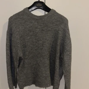 Grå stickad tröja från 157 - Mysig grå stickad tröja från 157 med rund halsringning och långa ärmar. Perfekt för lager-på-lager och chill dagar. Enkel design som funkar till allt och ger en avslappnad vibe.