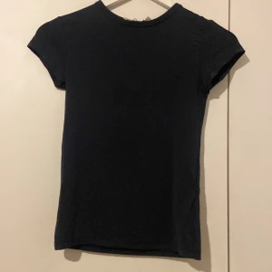 Marin blå basic tight t-shirt i silk - Enkel marin blå t-shirt med rund hals och korta ärmar. Modellen är rak och klassisk, perfekt att matcha med jeans eller kjol. Tillverkad i silk och mjuk tyg som känns skön mot huden. En riktig garderobsklassiker för dig som gillar stilrena plagg. Köpte den för 100kr men säljer den för 80kr