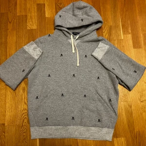 Unika Ralph Lauren Hoodie - Polo Ralph Lauren hoodie, grå med döskallebroderier, korta ärmar, huva och magficka. Tjockt unikt material – perfekt för höst/vinter. Storlek M.