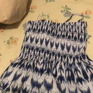 Blåvit smockad linnetopp - Supersöt blåvit linnetopp med smockad överdel och tunna axelband. Toppen har ett abstrakt mönster och är lätt utsvängd nertill för en luftig känsla. Perfekt för varma dagar och enkel att matcha med jeans eller shorts.