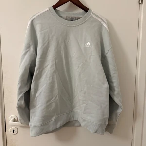 Mintgrön sweatshirt från Adidas - Säljer en mintgrön sweatshirt från Adidas med klassiska tre ränder på axlarna. Tröjan har en lös passform och är perfekt för en avslappnad stil. Adidas-loggan är tryckt på bröstet. Perfekt för kyliga dagar.