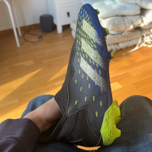 Fotbollsskor från Adidas - Snygga fotbollsskor från Adidas i blått och neongult med mönstrad ovansida. Skorna har en strömlinjeformad design med dobbar för optimalt grepp på planen. Perfekta för den som vill ha stil och funktion i ett.
