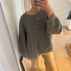 Grå stickad tröja - Säljer en mysig grå stickad tröja med rund hals och långa ärmar. Perfekt för kyliga dagar och enkel att matcha med olika outfits. Tröjan har en avslappnad passform och är tillverkad i en mjuk materialblandning.