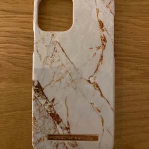 Marmormönstrat mobilskal från iDeal of Sweden - Snyggt mobilskal med marmormönster i vitt och brunt från iDeal of Sweden. Skalet har en elegant design med en guldig logotypdetalj. Perfekt för att ge din telefon ett stilrent utseende.