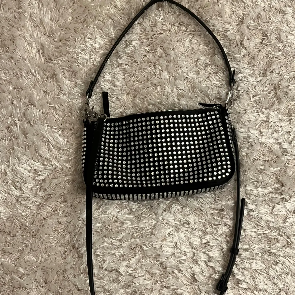 Snygg svart axelväska dekorerad med glittriga paljetter. Väskan har en justerbar axelrem och stängs med dragkedja. Perfekt för att ge en extra touch till din outfit.. Laukut & Käsilaukut.