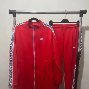 Röd träningsjacka från Nike - Snygg röd träningsjacka från Nike med dragkedja och vita detaljer. Jackan har långa ärmar och ett mönstrat band längs ärmarna. Perfekt för en sportig look!