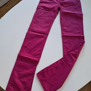 Rosa byxor från Armani Jeans - Snygga rosa byxor från Armani Jeans med dragkedja och knappdetaljer. Byxorna har en normal passform och är perfekta för att ge en färgklick till din outfit. De har en klassisk design med fickor både fram och bak. Obs! Långa.