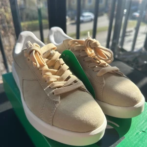 Beige sneakers från Diadora - Snygga beige sneakers från Diadora med snörning och rund tå. Skorna har en stilren design med en vit sula och är perfekta för en avslappnad stil. De är tillverkade i mocka och kommer i originalförpackning. Nypris 1199kr