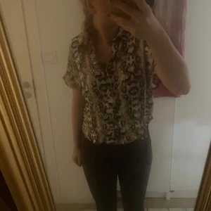 Mönstrad blus med ormskinn mönster - Säljer en snygg blus med ormskinn mönster i beige och bruna toner. Blusen har korta ärmar och en avslappnad passform. Perfekt för en trendig look. Storlek 40 men om du vill ha den som den sitter på mig passar den xs-s men om du vill ha den tightare så m-l