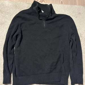 Svart stickad tröja med dragkedja - Säljer en svart stickad tröja med dragkedja vid halsen. Tröjan har långa ärmar och ribbade muddar vid ärmslut och nederkant. Perfekt för kyligare dagar.