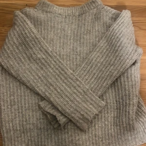 Grå stickad tröja från 157 - Säljer en mysig grå stickad tröja från 157. Tröjan har långa ärmar och en klassisk rund halsringning. Passar utmärkt till både jeans och kjol!