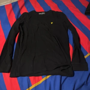 Svart långärmad tröja från Lyle & Scott - Säljer en stilren svart långärmad tröja från Lyle & Scott med deras ikoniska logga i gult på bröstet. Perfekt för en avslappnad och snygg look. Passar bra till både jeans och chinos. Använd 1-3 gånger. Säljer pga den inte är min stil längre.