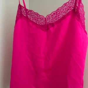 Rosa linne med spetsdetaljer - Säljer ett snyggt rosa linne med tunna axelband och vacker spetsdetalj längs halsringningen. Helt nyköpt med lapp kvar. Storleken är L men den är ganska liten så skulle nog mer säga S/M