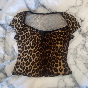 Leopardmönstrad topp med spetsdetaljer - Snygg leopardmönstrad topp med korta ärmar och spetsdetaljer vid halsringningen. Toppen har en liten knytrosett framtill och är perfekt för en trendig look.