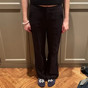 Svarta kostymbyxor - Snygga svarta kostymbyxor med låg midja och en klassisk rak passform. Perfekta för en stilren look. Byxorna har en diskret dragkedja och knapp framtill.