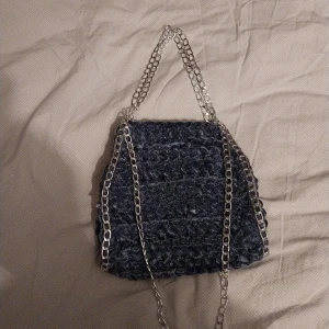 Blå virkad väska med silverkedja - Snygg blå virkad handväska med en snygg kedja som hantag. Perfekt för att ge din outfit en unik touch. Väskan har en mjuk textur och en modern design.