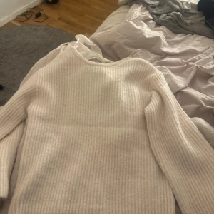 Vit ribbad tröja med rosett - Säljer en mysig vit ribbad tröja med en söt rosett i nacken. Perfekt för kyliga dagar och ger en stilren look. Tröjan har långa ärmar och en rund halsringning.