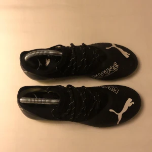 Svarta fotbollsskor från Puma - Snygga svarta fotbollsskor från Puma med vit logga och limegröna dobbar. Skorna har snörning och är designade för optimal prestanda på planen. Perfekta för den som vill ha stil och funktion i ett. Använd 3 gånger. Ord pris 1200kr. Köpt på unisport.