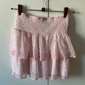 Rosa blommig kjol från Vero Moda - Söt rosa blommig kjol från Vero Moda med volanger och elastisk midja. Perfekt för en somrig look. Kjolen har ett luftigt och lätt material som ger en skön känsla.🩷