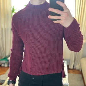 Vinröd stickad tröja från Crocker - Säljer en vinröd stickad tröja från Crocker. Tröjan har långa ärmar och en snygg snörningsdetalj på sidorna. 