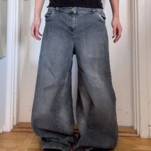 Grå baggy jeans - Säljer ett par grå baggy jeans med breda ben och klassisk femficksdesign. Jeansen har en knappgylf och är perfekta för en avslappnad stil. Perfekt för dig som gillar en loose fit.