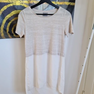 Beige och vit klänning från Vero Moda - Snygg klänning från Vero Moda i beige och vit. Överdelen är stickad och kortärmad medan nederdelen är i ett lättare material. Perfekt för en stilren look.