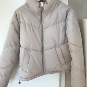 Beige puffer jacka Stl XS - ljus kitt beige pufferjacka / vadderad jacka med stå krage och dragkedja framtill. Sidfickor och dragsko i sidorna. H&M Divided Stl XS, passar en small bra. Använd ett fåtal gånger är i mycket bra skick, inga defekter.  Nypris: 399:-